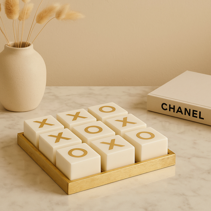 Luxury white and gold noughts and crosses set on marble table with vase and Chanel book