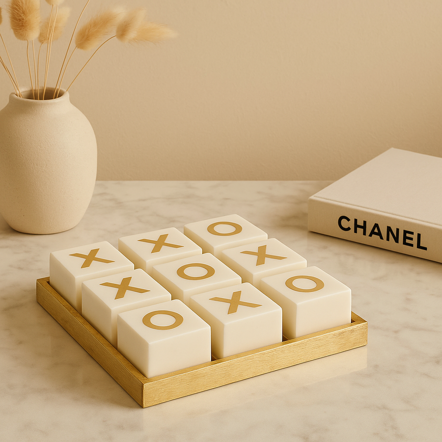 Luxury white and gold noughts and crosses set on marble table with vase and Chanel book