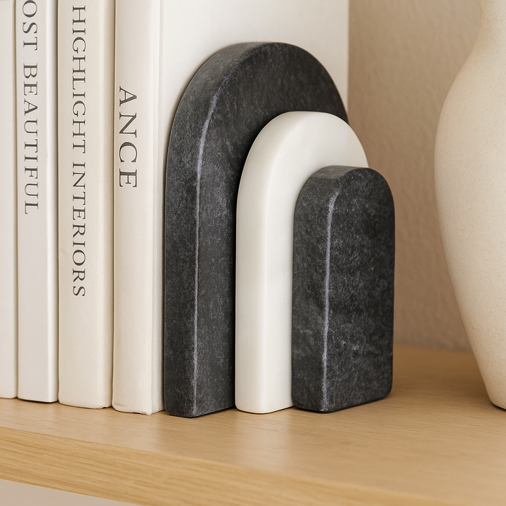 Close-up of black and white marble arch bookends holding books on a wooden shelf with a neutral ceramic vase
