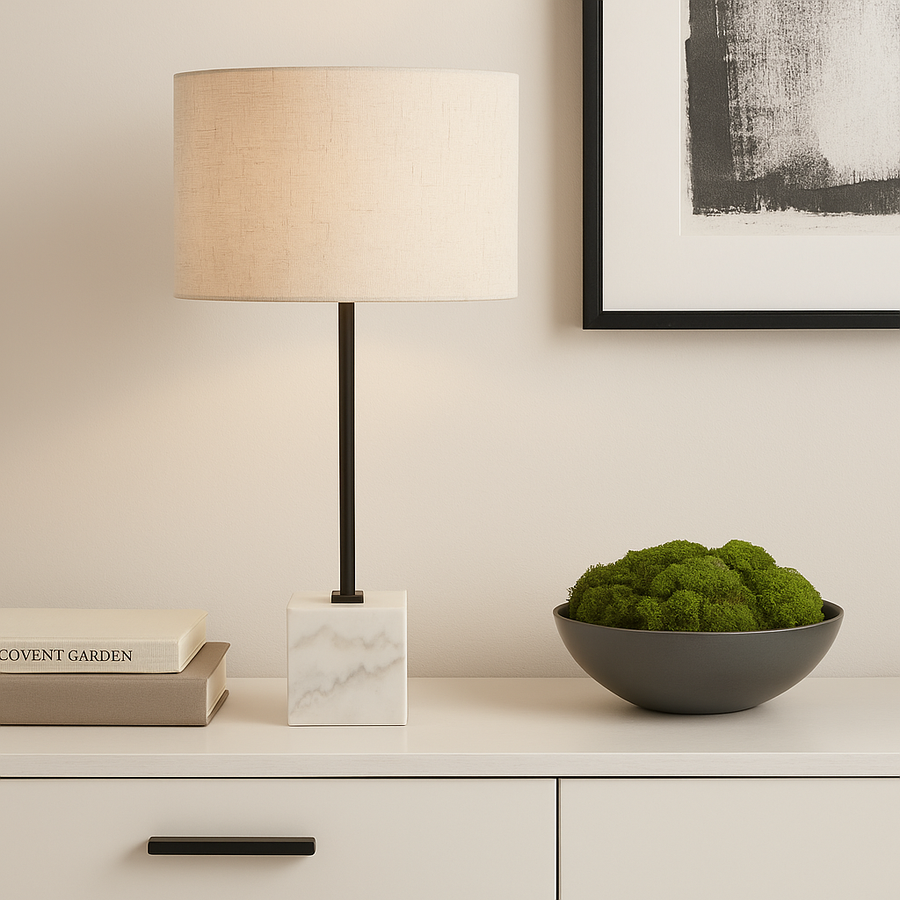 Modern table lamp with marble base and beige linen shade styled on a white sideboard with books, monochrome artwork, and a moss bowl