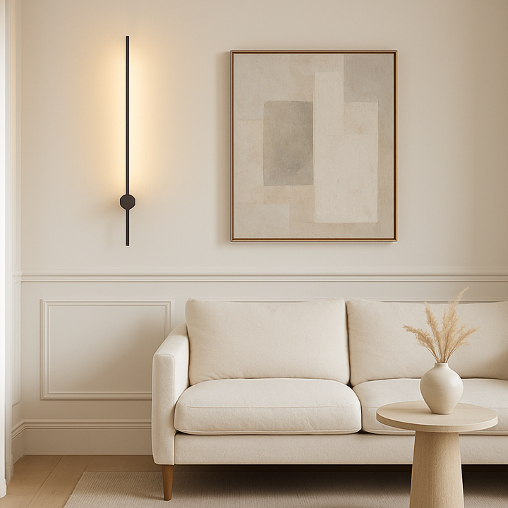 Luxury living room with a modern 90cm black stick wall light on white panelled walls, styled with a cream sofa, neutral abstract artwork, and a round side table with a ceramic vase.