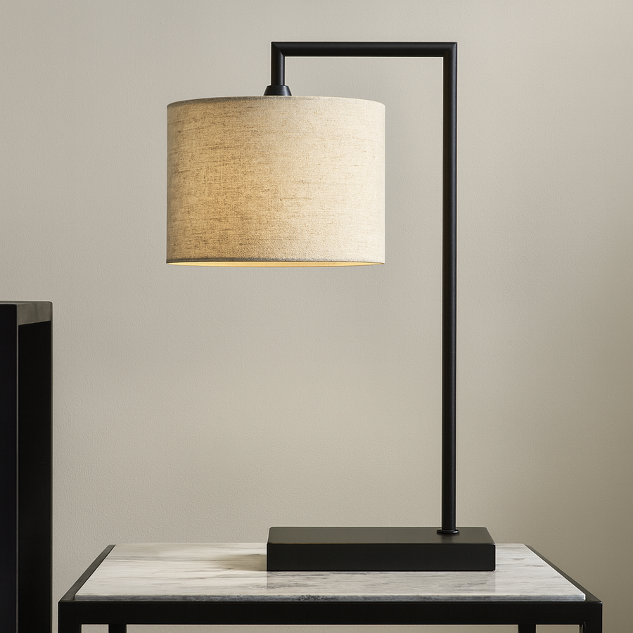 Luxury modern table lamp with black frame and 25cm natural linen shade on a marble side table against a light wall.