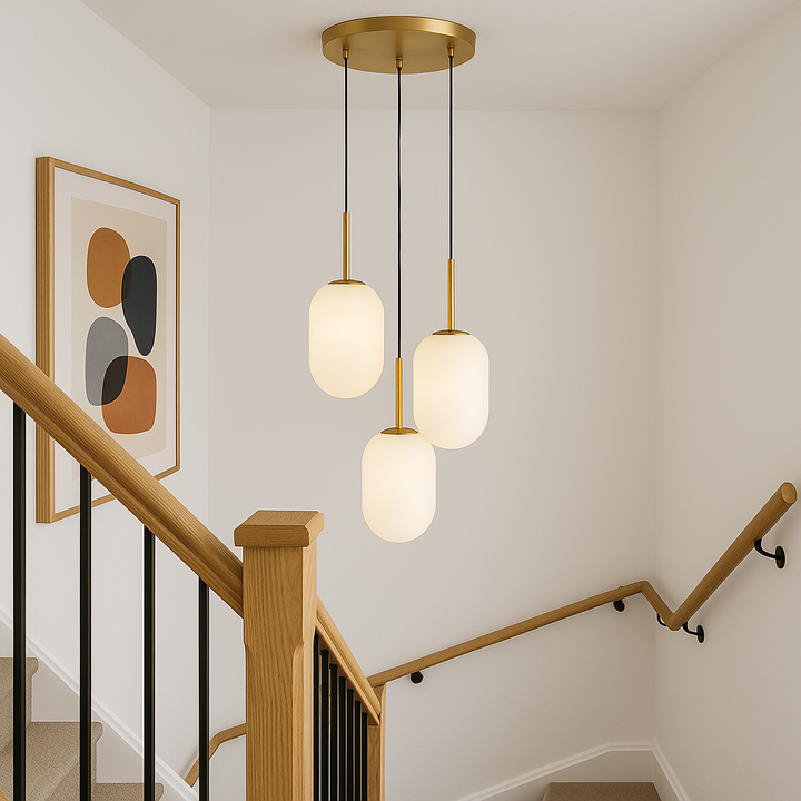 Luxury modern 3 light gold pendant with frosted glass shades hanging at the top of a staircase with white walls, oak and black railings, and abstract modern artwork.