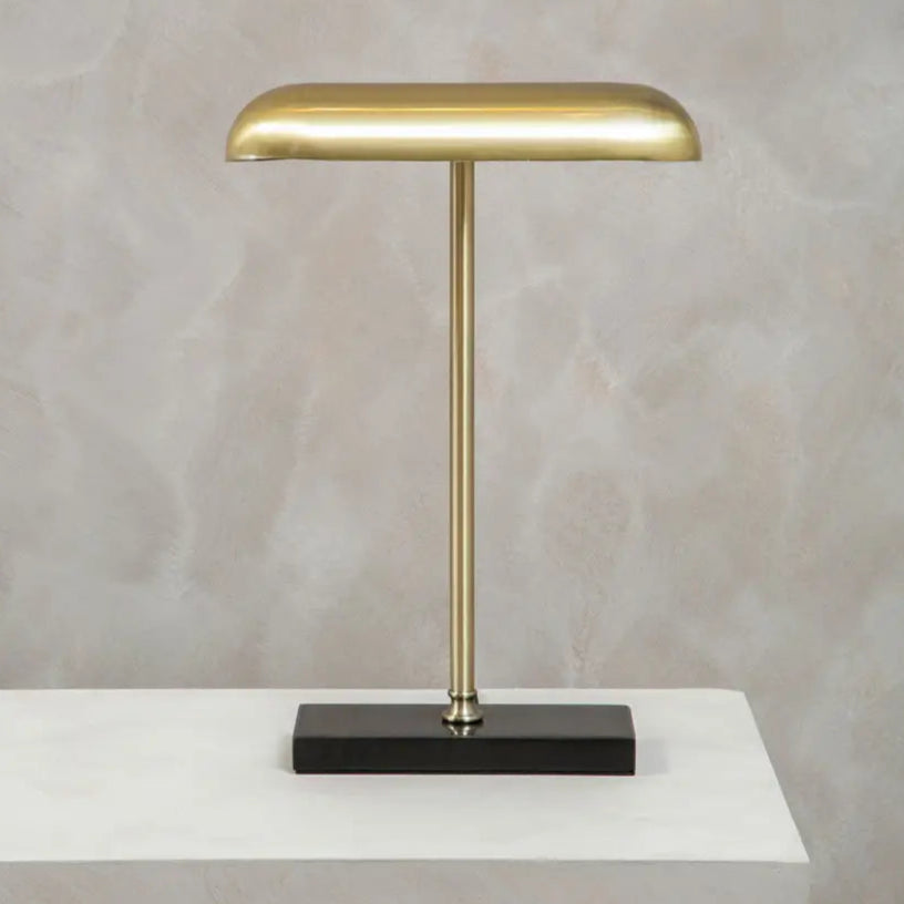 Gold desk lamp on a black base with a neutral background