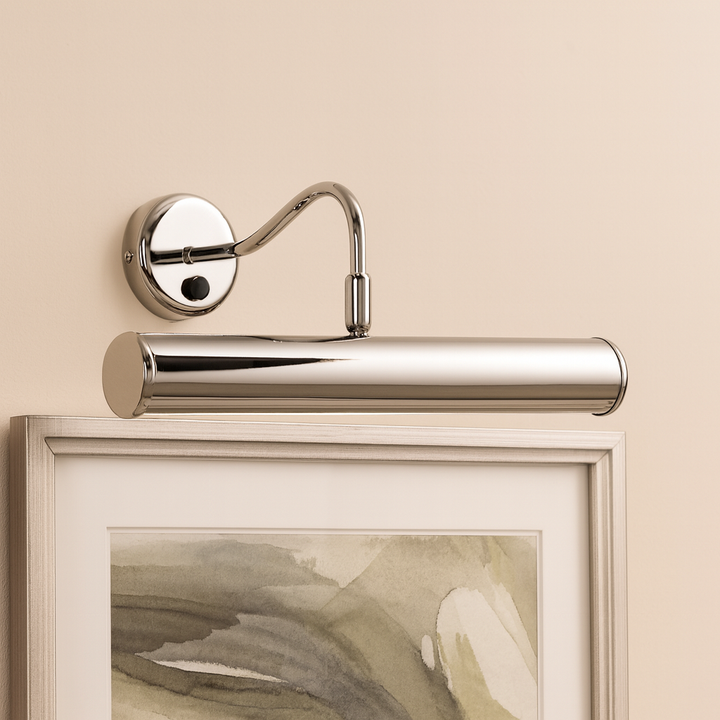 Polished chrome picture wall light illuminating framed abstract artwork on a neutral beige wall