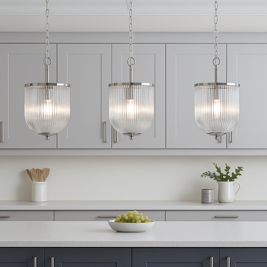 Three ribbed glass pendant lights with chrome fittings hanging above a modern kitchen island with full cabinet backdrop and silver accents.