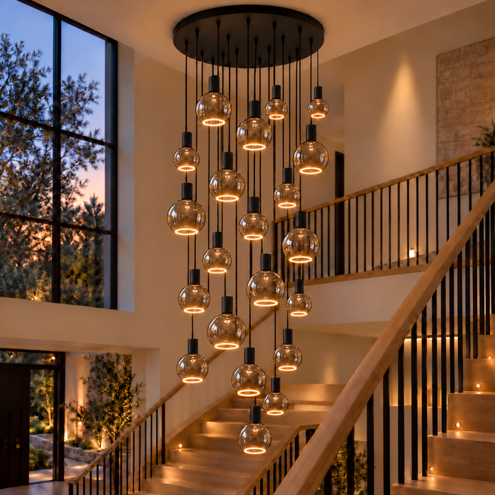 Roma 21-light pendant with black caps and smoked glass bulbs in three sizes, illuminated by warm bottom halo rings above an oak staircase.