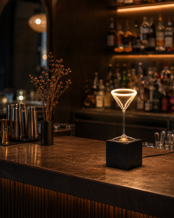 Roma Cocktail Glass Aura Ring table lamp with black wooden block base and visible power cable on the edge of a luxury cocktail bar counter.
