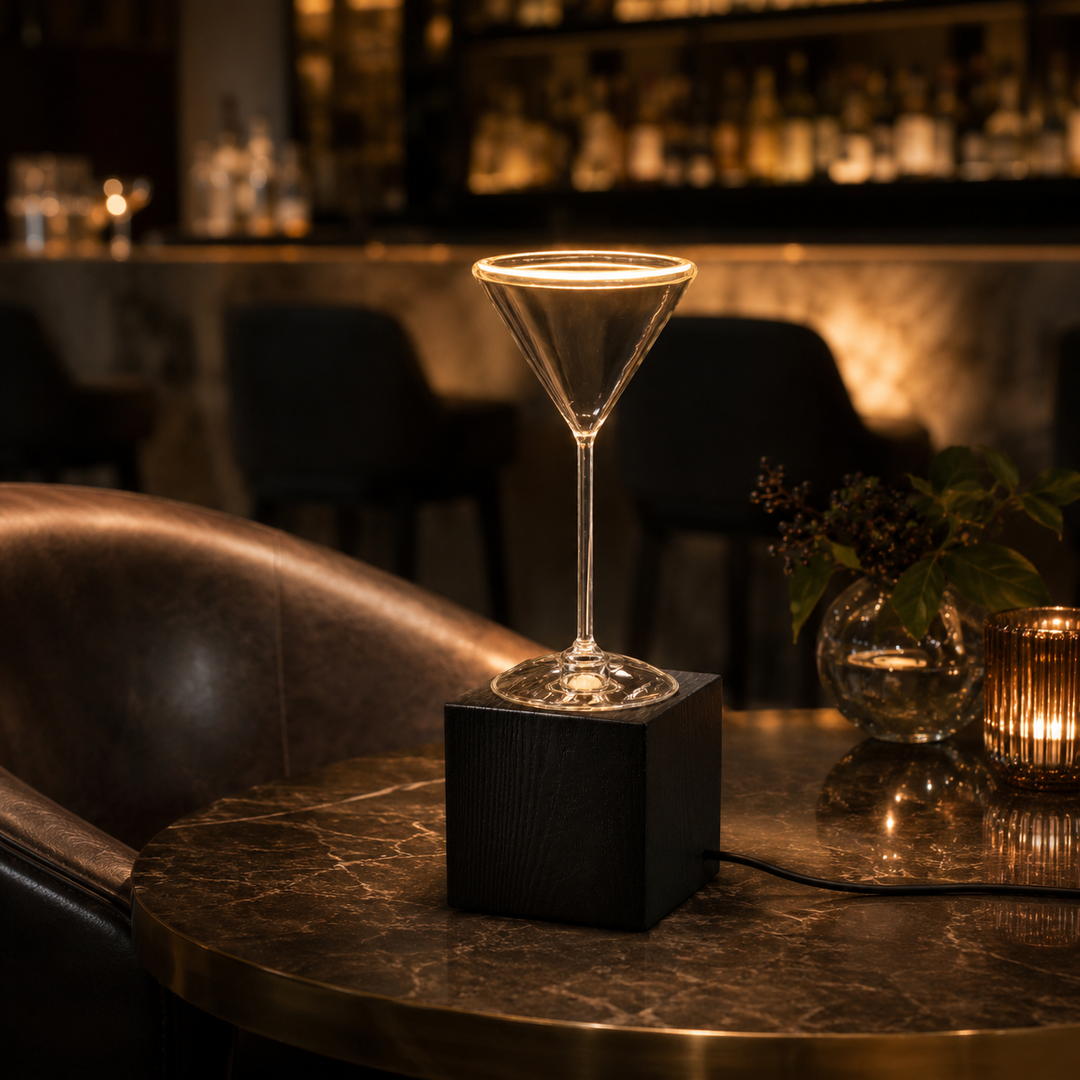 Roma Cocktail Glass Aura Ring table lamp with black wooden block base and visible power cable on a luxury bar table with warm ambient lighting.
