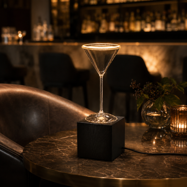 Roma Cocktail Glass Aura Ring table lamp with black wooden block base and visible power cable on a luxury bar table with warm ambient lighting.