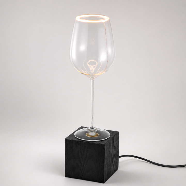 Roma wine glass aura ring table lamp with black wooden base and visible black power cable, illuminated with warm 2200K glow.