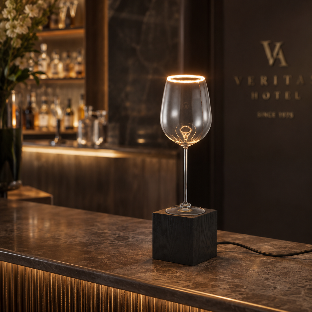 Roma wine glass table lamp with black wooden base glowing on a stylish bar counter in a hospitality setting