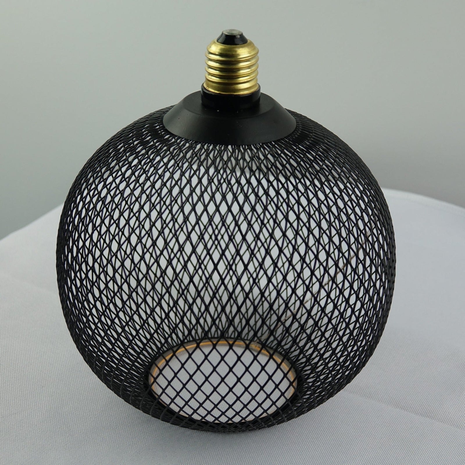 Black mesh light fixture on a white surface with a gray background