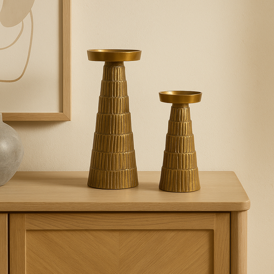 Set of two gold metal candlesticks with ridged design, tall and small sizes displayed on a modern oak sideboard in a luxury neutral home interior