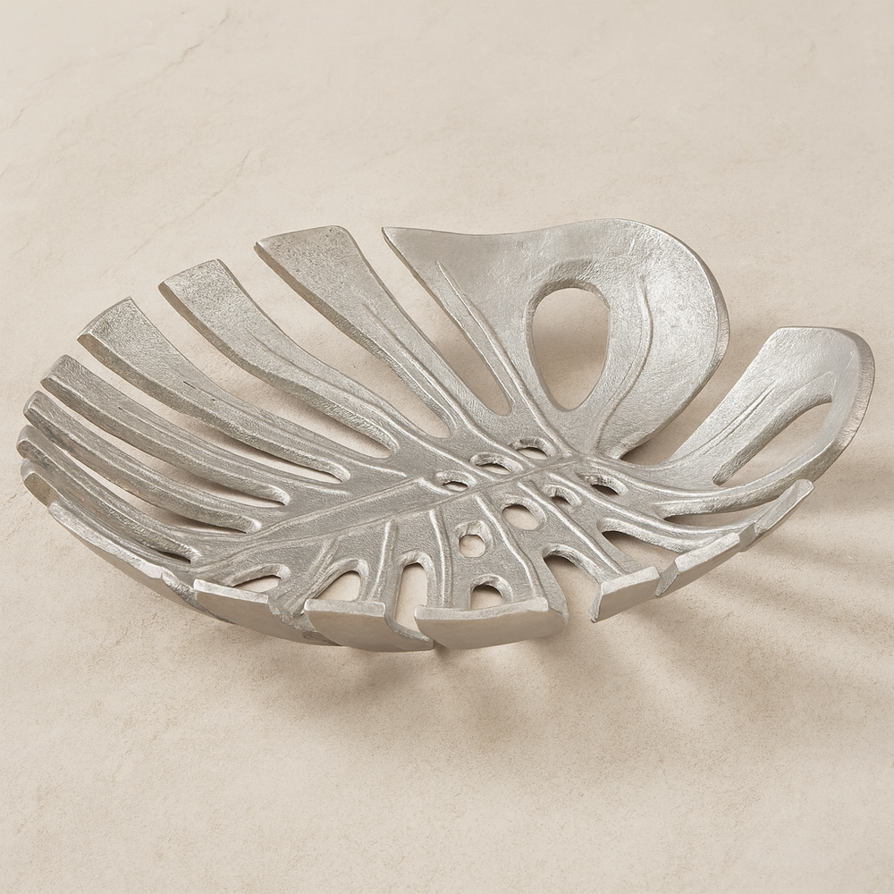 Luxury silver monstera leaf decorative dish with openwork design styled on light neutral marble surface