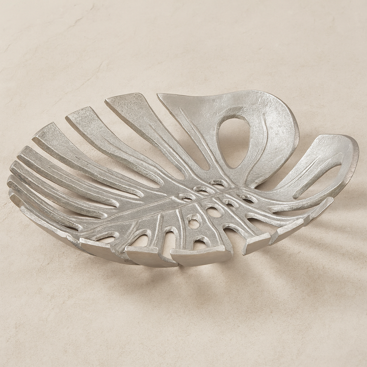 Luxury silver monstera leaf decorative dish with openwork design styled on light neutral marble surface