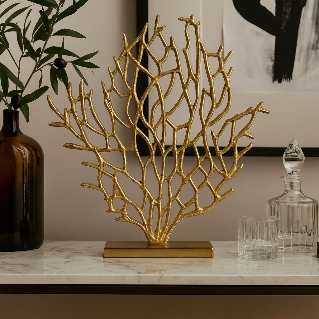 Gold coral-like decorative piece on a marble surface with a vase and decanter in the background.