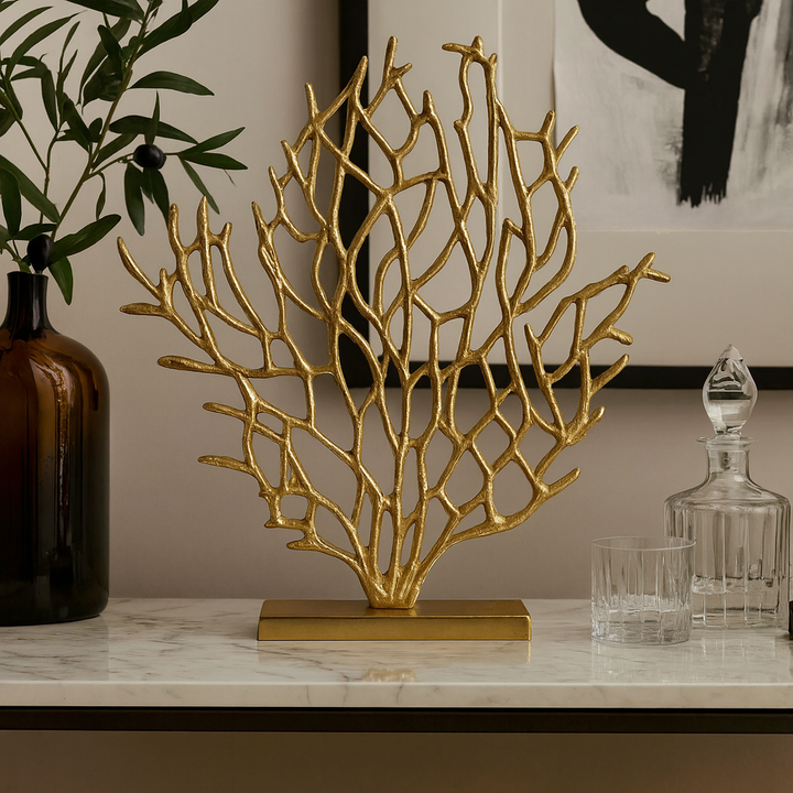 Gold coral-like decorative piece on a marble surface with a vase and decanter in the background.