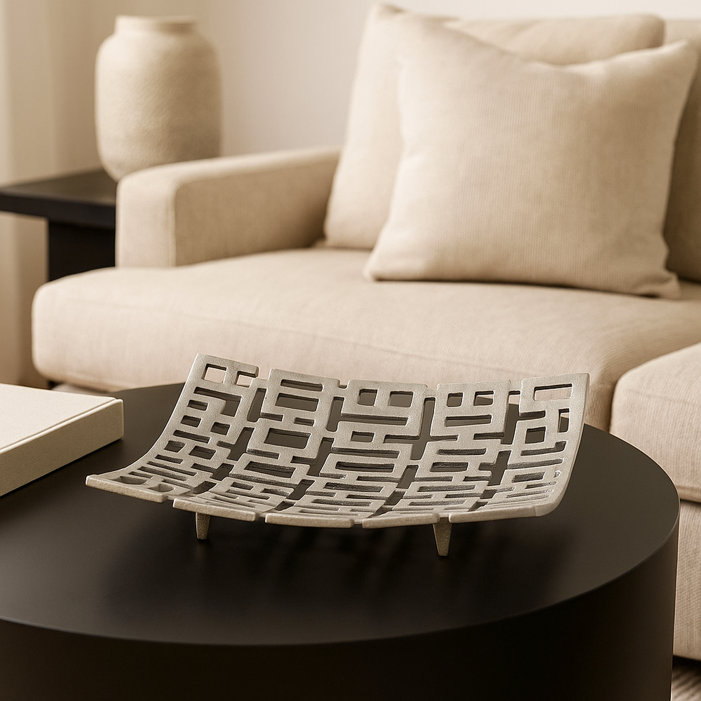 Silver geometric decorative bowl styled on a sleek black coffee table in a modern living room with neutral beige sofa
