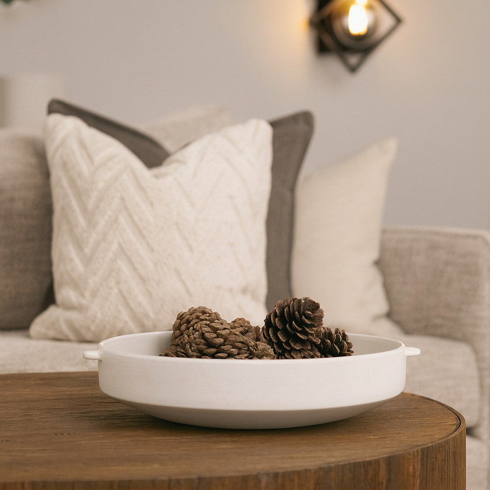 White ceramic decorative bowl styled on a wooden coffee table with pinecones in a modern neutral living room