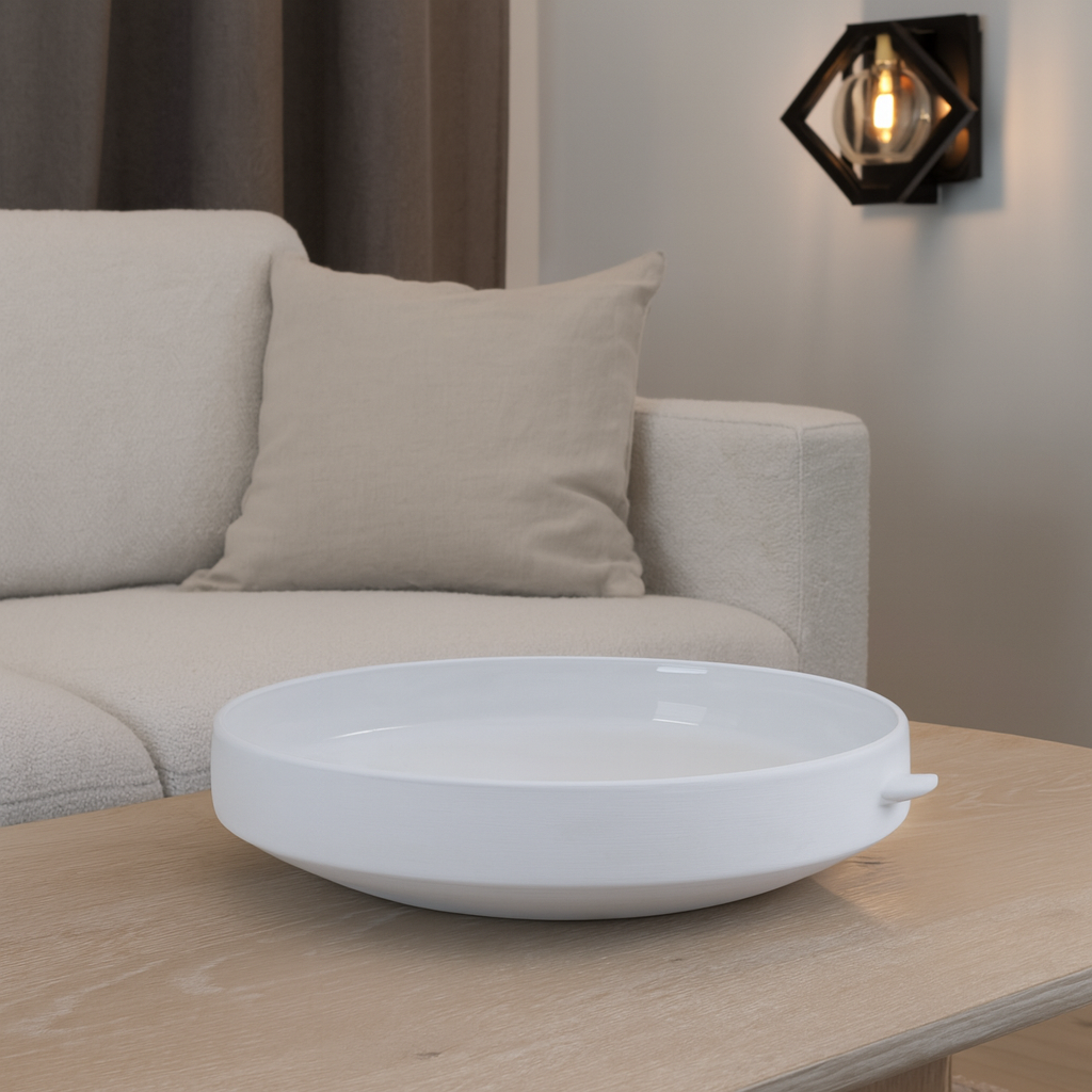 Modern white ceramic decorative bowl styled on a light wooden coffee table in a neutral living room with beige sofa and wall light