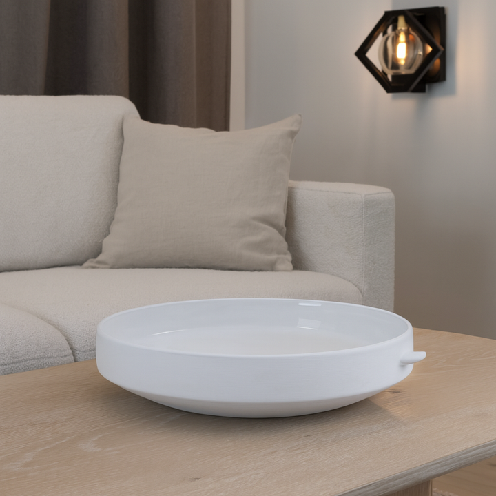 Modern white ceramic decorative bowl styled on a light wooden coffee table in a neutral living room with beige sofa and wall light