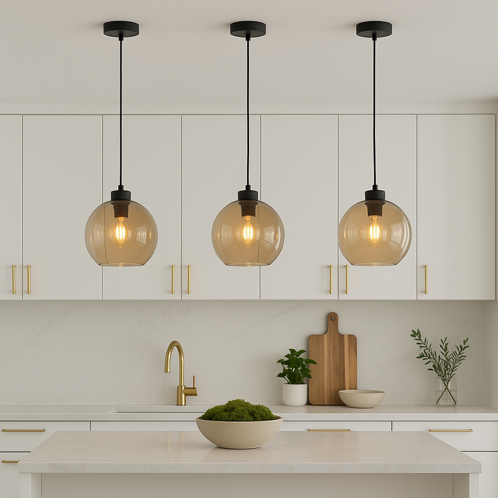 White kitchen with gold accents featuring three 25cm amber glass pendant lights hanging above an island with moss bowl