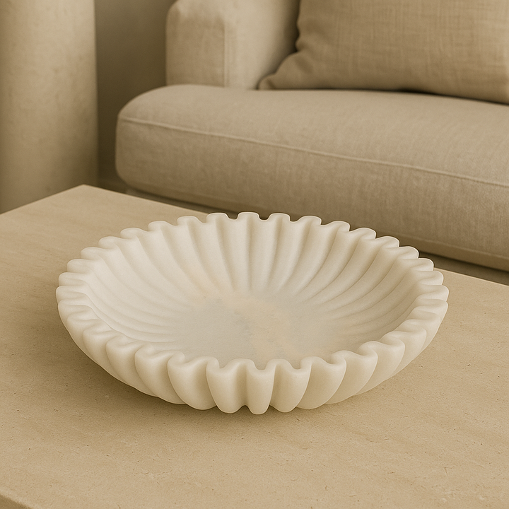 Luxury lifestyle image of a white marble scalloped bowl styled on a beige stone coffee table in a modern neutral living room