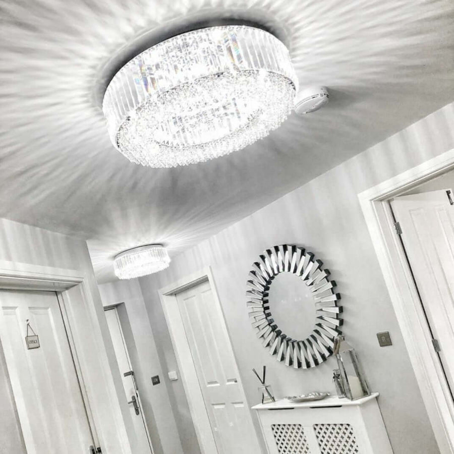 A polished chrome ceiling light with rectangular crystal pieces and a skirt of crystal buttons, installed in a room with white walls and doors.